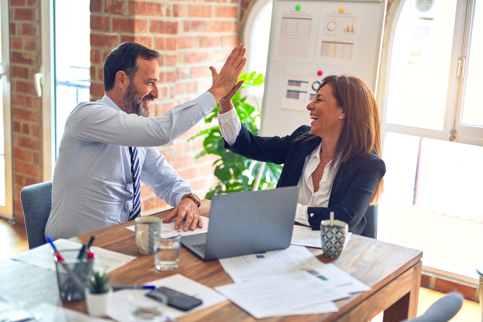 man in white dress shirt sitting beside woman in black long sleeve shirt giving a high five